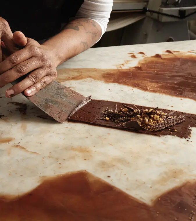 black-man-chief-collects-cooled-melted-chocolate-from-marble-table-closeup-abstract-picture-working-chocolate-confectionery
